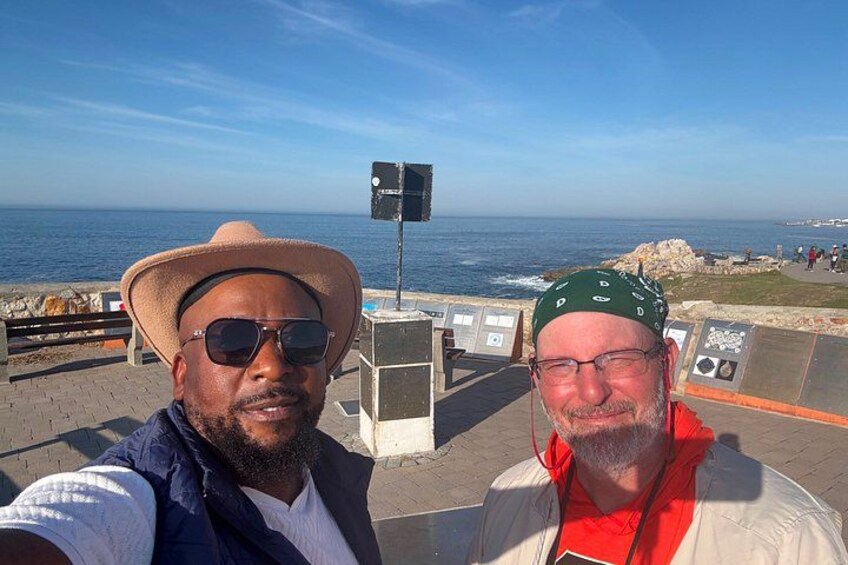 Two people taking a selfie with a coastal view and informational signs in the background. 5