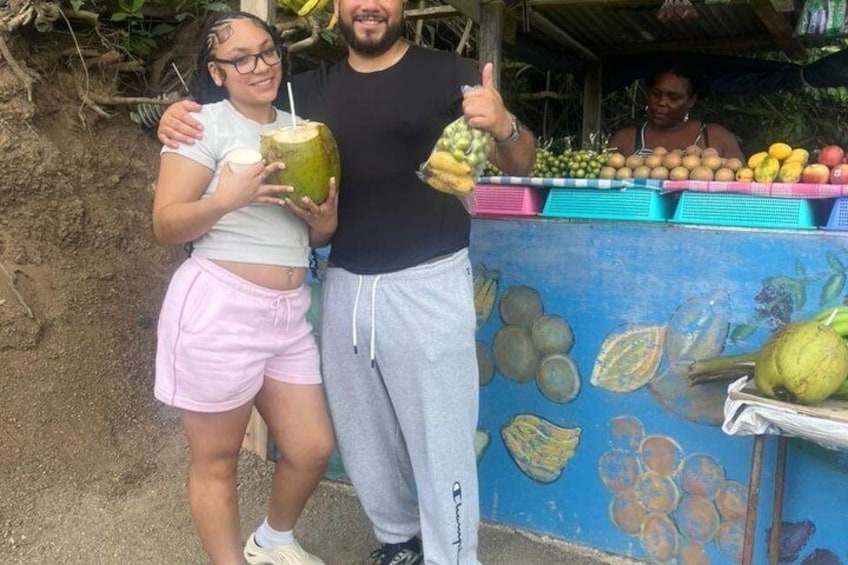 Two people holding coconuts, a fruit stand with bananas and apples, and a mural with fruits. 2