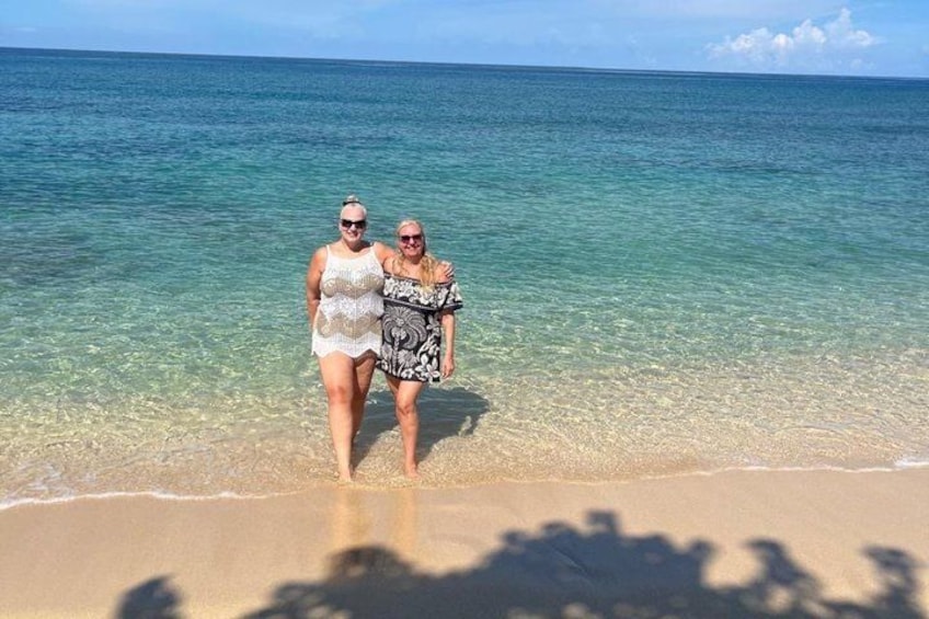 Two people walking on a beach with clear blue water. 1
