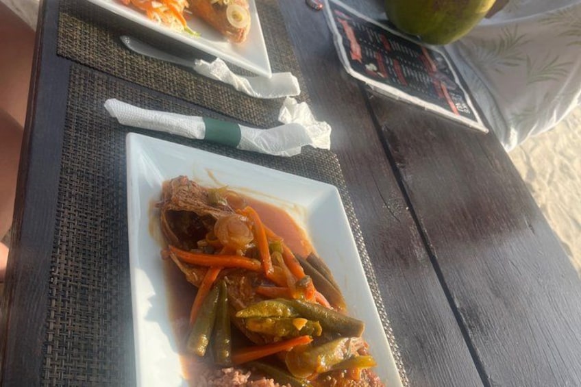A meal on a wooden table with a woven placemat, a plate of food, and a menu. 3