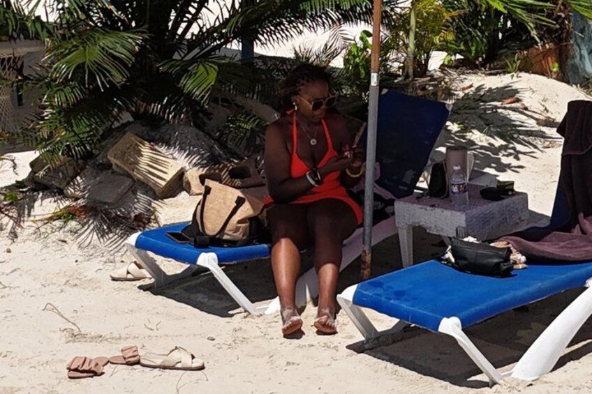 A person sitting on a beach chair, a blue lounge chair, and a beach umbrella. 4