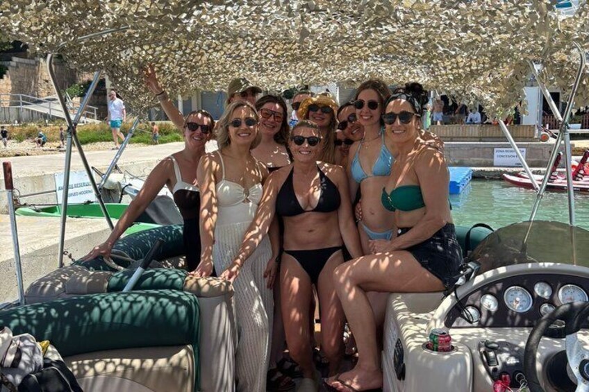 A group of people on a boat with a steering wheel and a green cover. 5
