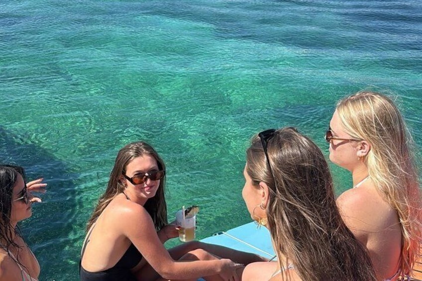 Four people sitting by a clear blue sea, one holding a drink. 2