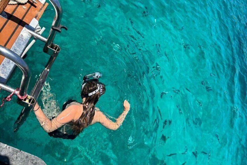 A person swimming in clear blue water with a wooden deck and metal ladder in the background. 4