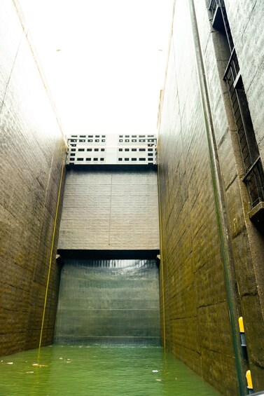 A large concrete structure with a water-filled interior and a metal grid at the top. 3
