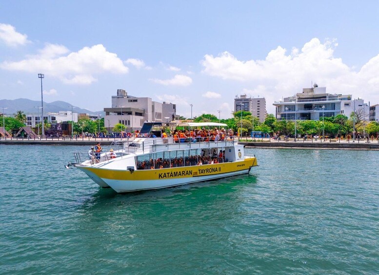A yellow and white boat named 'Katamaran Tayrona II' on calm waters with a cityscape in the background. 1