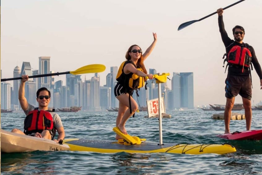 People on paddleboards in a body of water with a city skyline in the background. 1