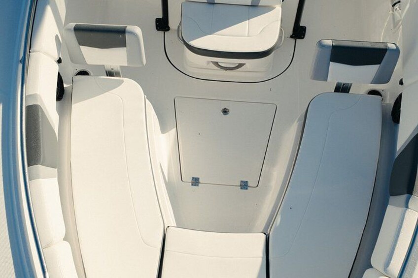 A boat's interior with white cushioned seating and a central control panel. 1