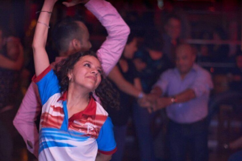 A person dancing with raised arms in a crowded indoor setting. 3