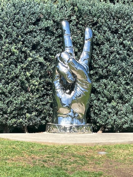 A metallic peace sign sculpture with 'PEACE & LOVE' inscribed at its base, set against a backdrop of dense green foliage. 4