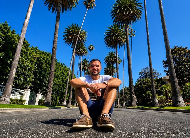 A man sitting on a paved road with palm trees in the background. 3