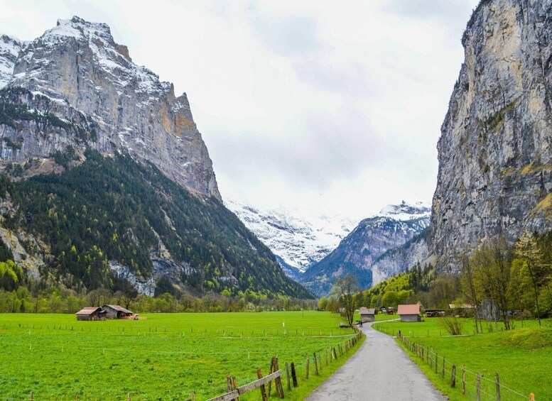 A valley with green fields, wooden fences, and houses, flanked by snow-capped mountains. 4
