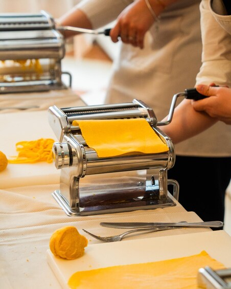 A person using a pasta machine to roll out dough. 2
