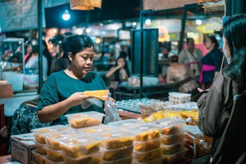 A person purchasing food at a market stall with various packaged goods on display. 5