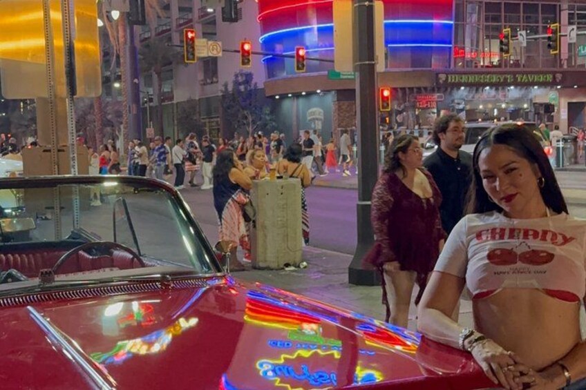 A red vintage car with neon lights, a crowd of people, and a building with colorful lights in the background. 4