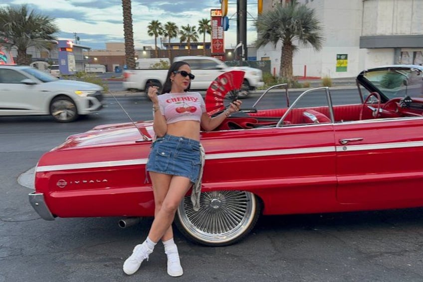 A red convertible car parked on a street with palm trees and buildings in the background. 2