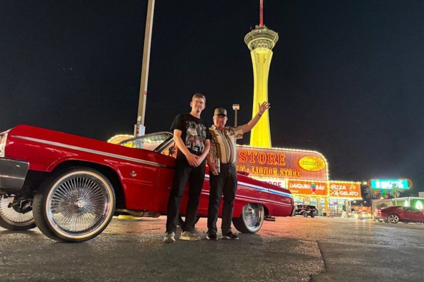 A red vintage car, a tall tower, and a brightly lit store at night. 5