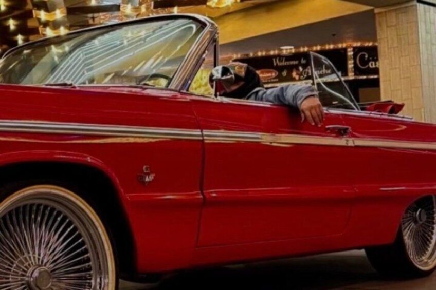 A red vintage car parked indoors with a person leaning on the door. 4