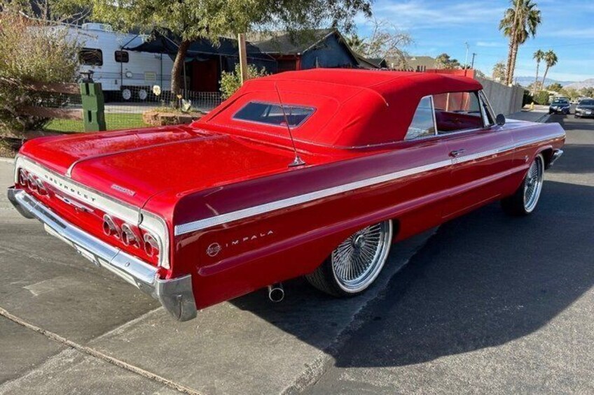 A red vintage Impala with chrome wheels parked on a paved surface. 2