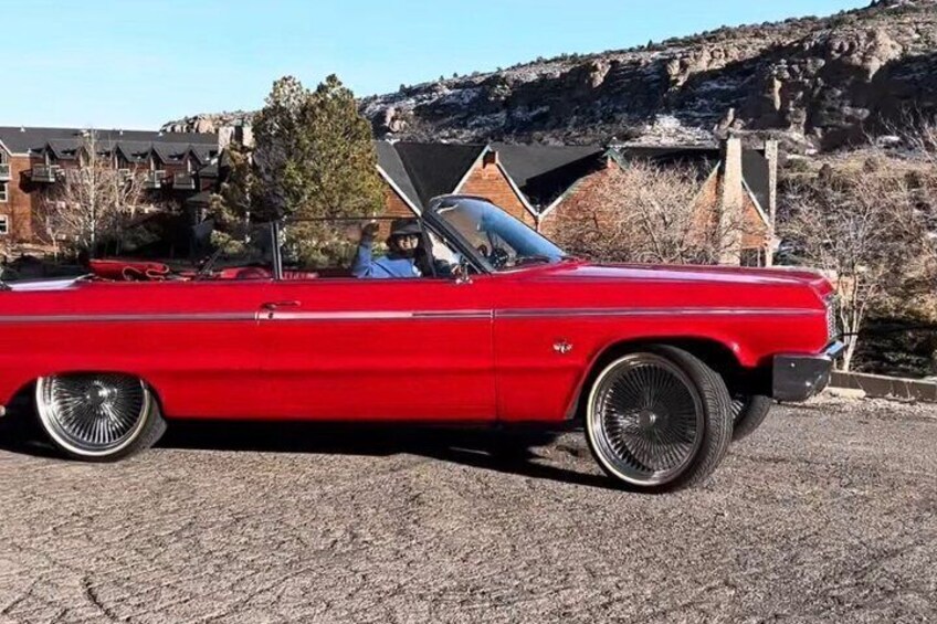 A red classic car parked on a paved surface with a mountainous background. 5