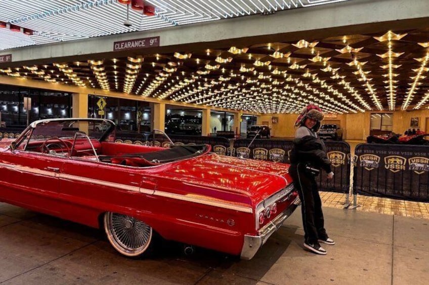 A red vintage car in a museum with a person standing beside it. 1