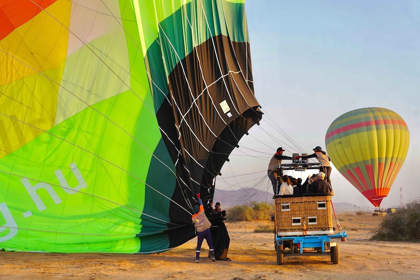 A large colorful hot air balloon being prepared for launch with people on a basket. 3