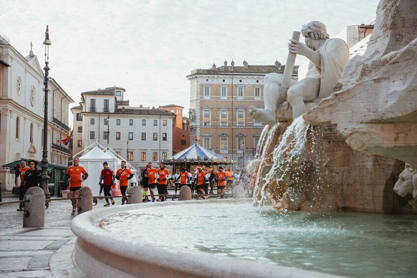 A fountain with a statue, a group of runners, and historic buildings in the background. 1