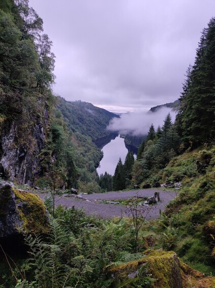 A mountainous landscape with a lake, dense forest, and a rocky cliff. 4