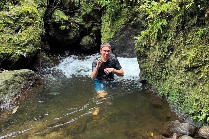 A person wading in a clear stream surrounded by moss-covered rocks and greenery. 2