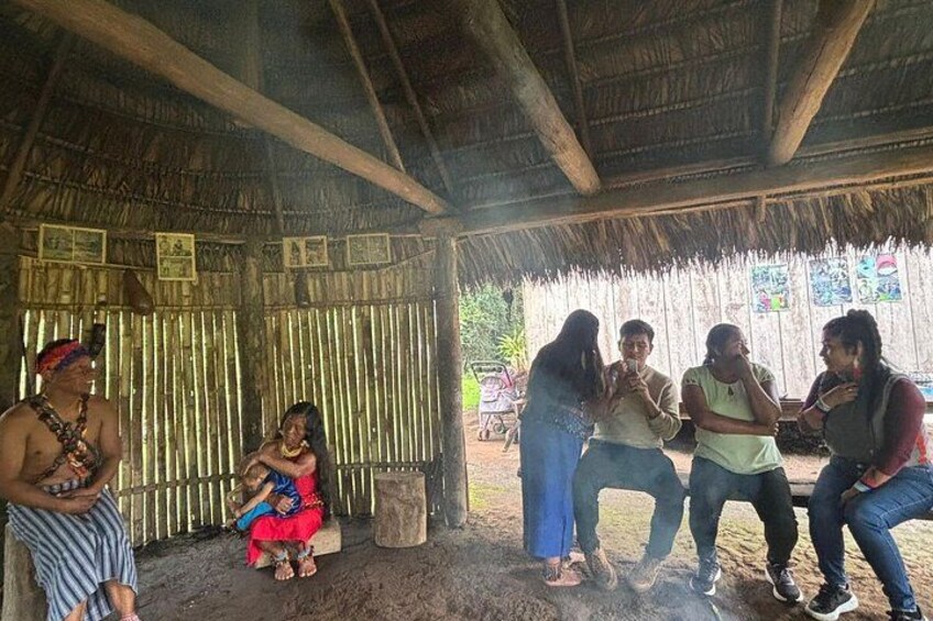 A group of people in a rustic outdoor setting with a thatched roof structure. 4