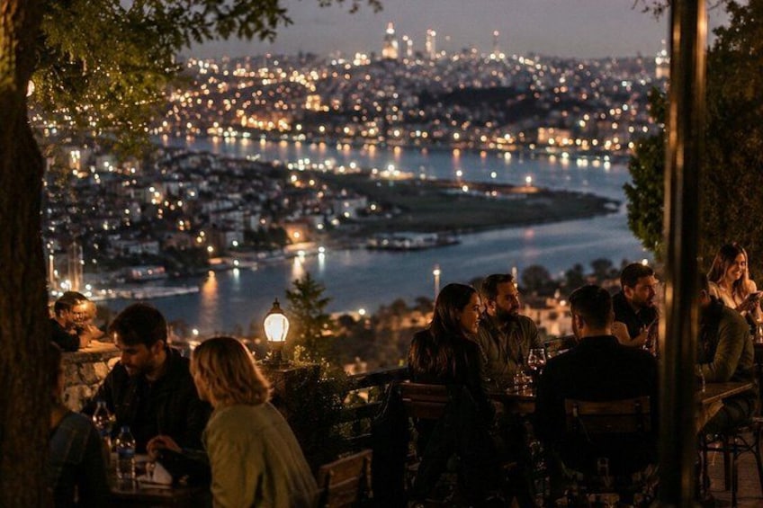 A group of people dining at an outdoor restaurant with a cityscape and river in the background. 2