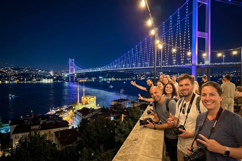 A group of people taking a photo with a bridge and city lights in the background. 1