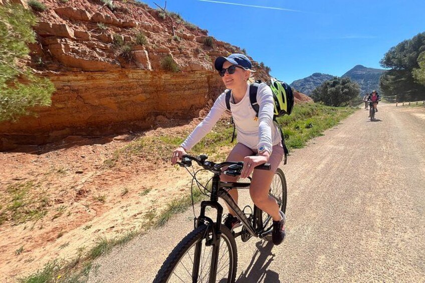 A person riding a bicycle on a gravel road with a rocky hillside and sparse vegetation in the background. 2