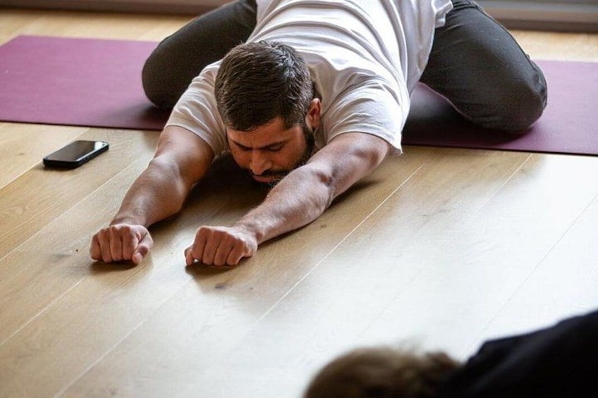A person lying prone on a wooden floor with a purple mat, a smartphone, and a black object nearby. 2