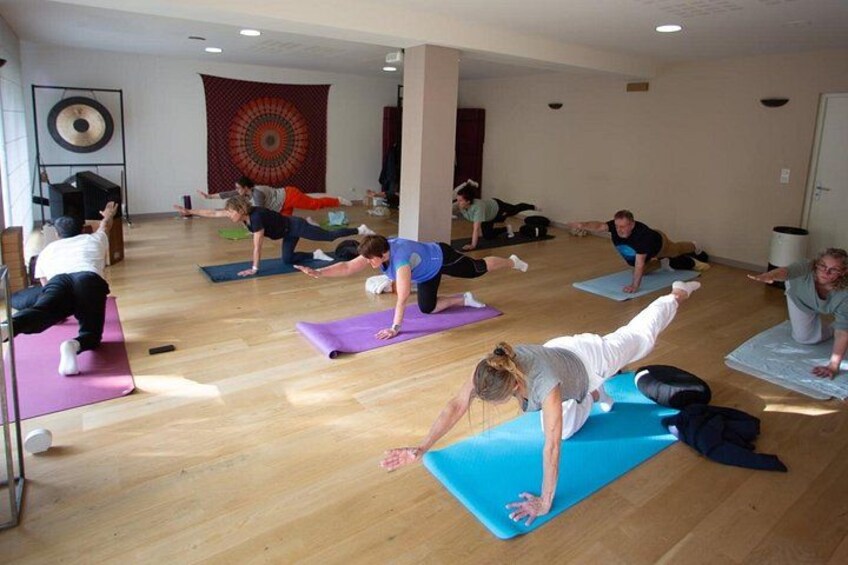 A group of people doing a yoga class on mats in a room with wooden floors and a tapestry on the wall. 3