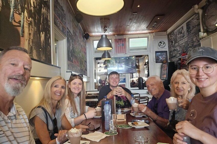 A group of people sitting at a wooden table in a restaurant with posters on the walls. 2