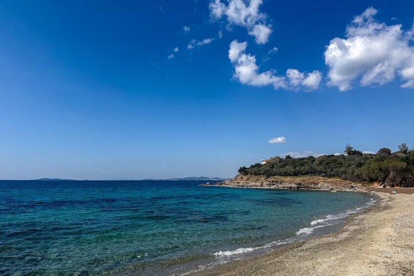 A beach with clear blue water, a sandy shore, and a forested hill in the background. 4