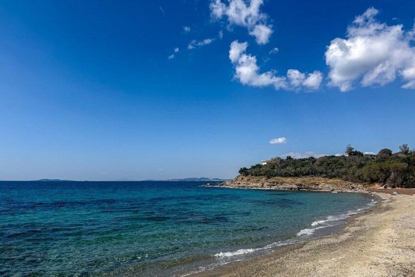 A beach with clear turquoise water, a sandy shore, and a forested hill in the background. 3