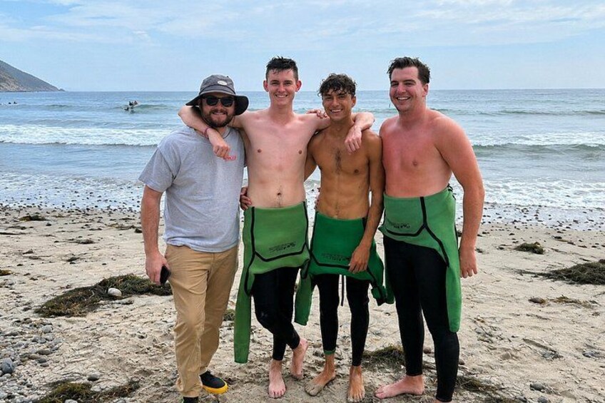 A beach with people wearing wetsuits and a person in a hat. 3