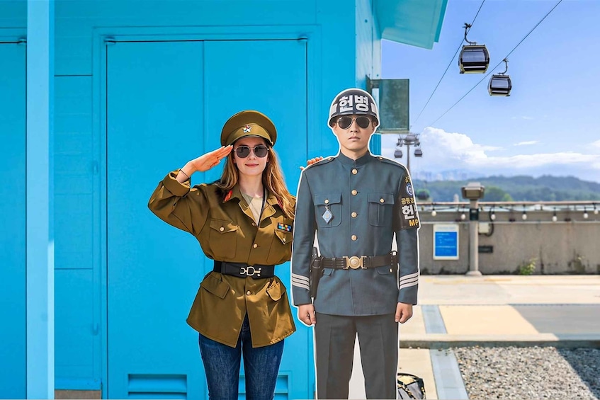 Dos personas con uniforme militar de pie frente a un edificio azul, con un teleférico al fondo. 3