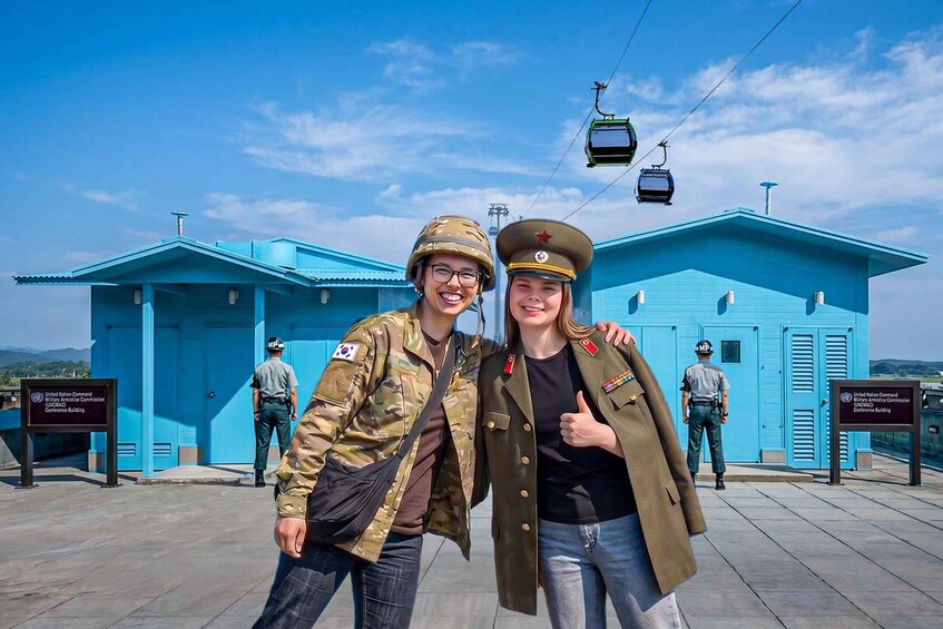 Two people in military uniforms standing in front of a blue building with a sign that reads 'United States Army Command and Control Conference Building.' 1