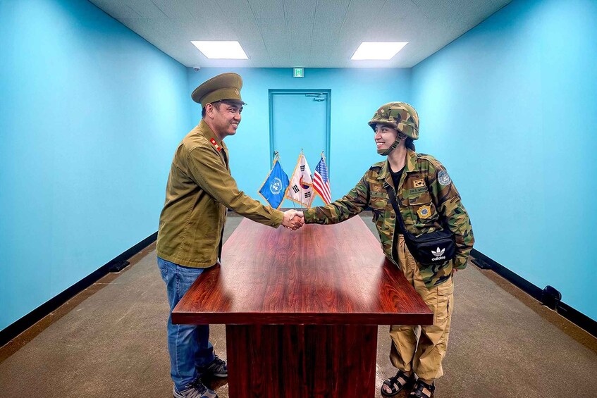 Two individuals in military uniforms shaking hands in a room with blue walls and a wooden table. 4