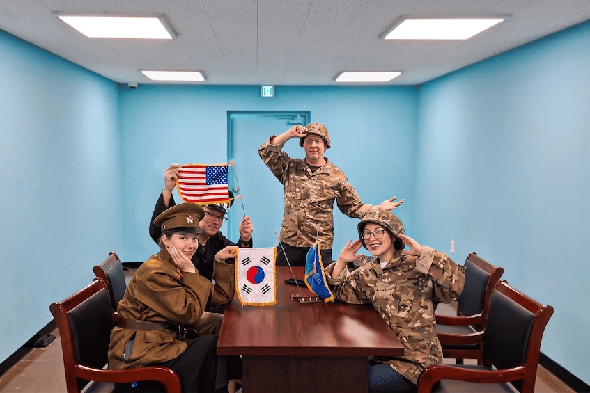 Cuatro personas con uniforme militar sentadas alrededor de una mesa con la bandera de Corea del Sur, la bandera de Estados Unidos y la bandera de Corea del Norte. 2