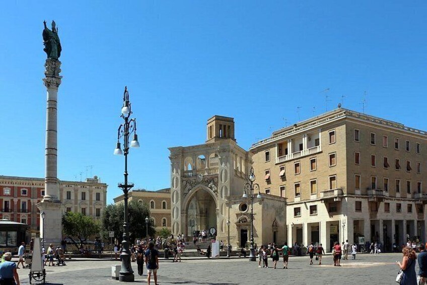 A public square with a central monument, surrounding buildings, and people walking. 4