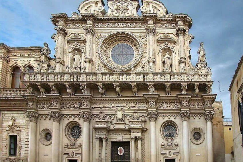 A detailed facade of a historic building with ornate sculptures, a large circular window, and a central door. 3