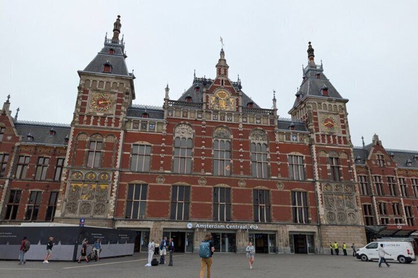 A historic building with intricate architecture, a prominent clock tower, and a sign for Amsterdam Centraal station. 5