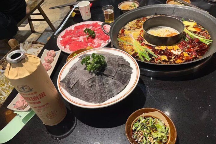 A table with various dishes, including a hot pot, raw meat, and a bowl of greens. 3
