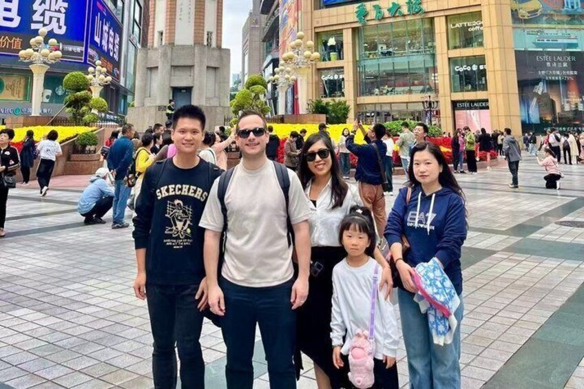 A group of people in a public square with buildings and shops in the background. 2