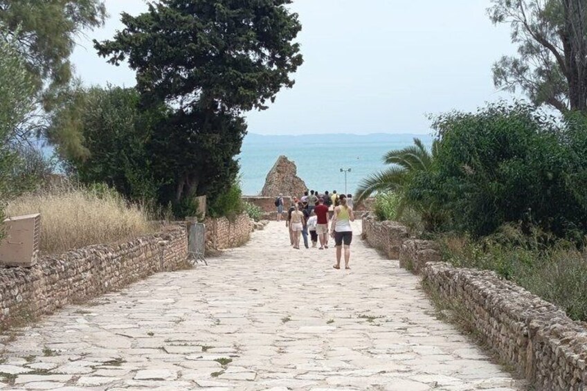 A stone pathway leading to a coastal area with a group of people walking. 2