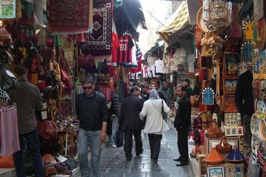 A crowded market with people walking through narrow aisles lined with various goods. 3